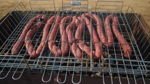 Long Raw Sausages Lie On Hot Coals On A Grill Or Barbecue During A Picnic Outdoors