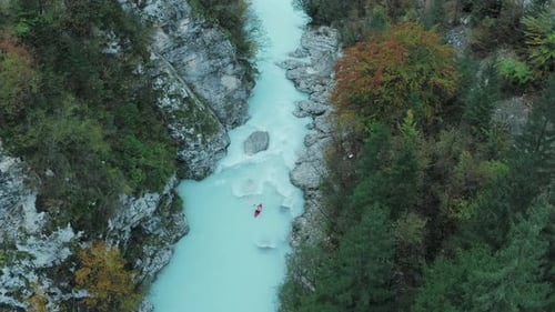 Top-down aerial view of a man kayaking on a red kayak or canoe in the middle of an blue river