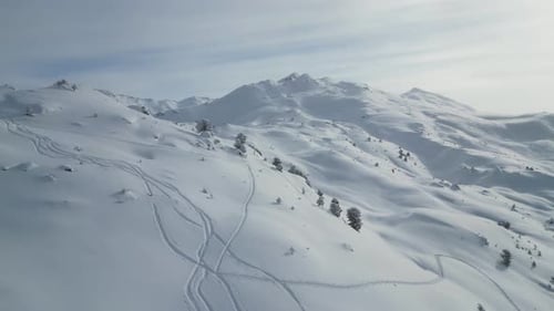 Aerial epic snow covered glacier mountain range scenery, fllying over alpine summits with ski tracks