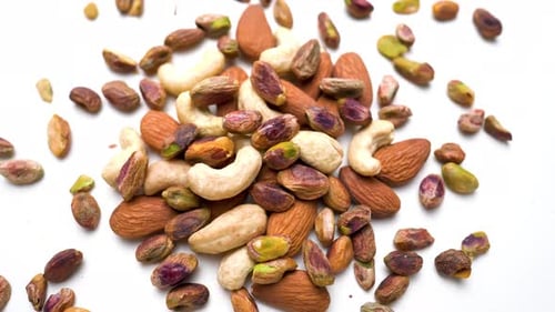 Scattered Pistachio And Cashew Nuts Rotating View On White Table Background