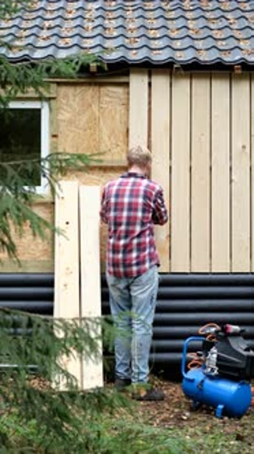 Mann im karierten Hemd montiert Holzpaneele an der Außenwand