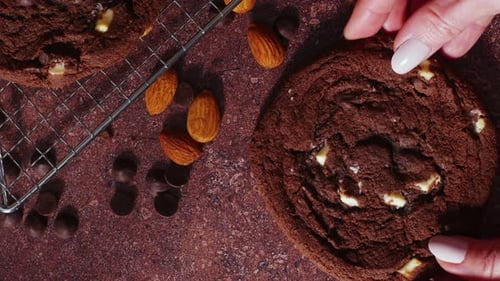 Hand Placing Fresh Cookie With Almonds on Rustic Table for Bakery Shop Display