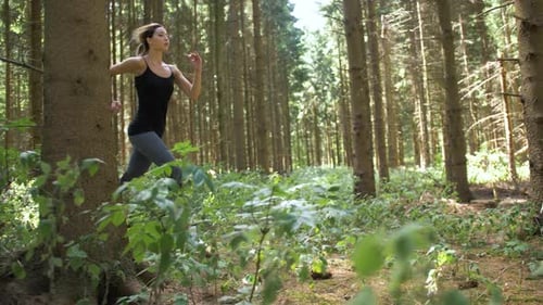 Woman begins running through wooded area with long prancing stride. Cardio health and fitness outsid