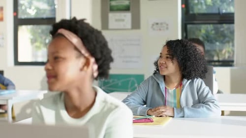 African American teen girls turning toward teacher after prompt in classroom smiling with notebook