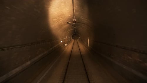 Railroad Tracks and Running Train in Tunnel Near Electric Poles in Dark Night