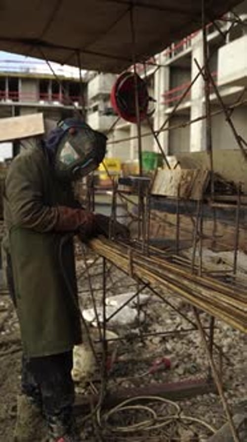 Welder creating sparks on rebar frame at construction site, vertical