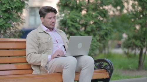 Man Using Laptop on Park Bench Outdoors