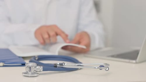 Close up of Stethoscope, Doctor Reading Book in Background