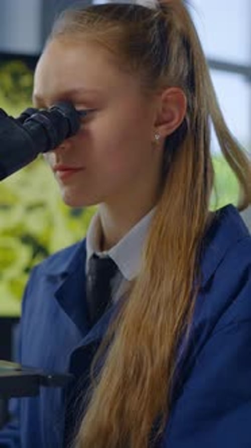 Teenage Girl Looks Through Microscope in Laboratory