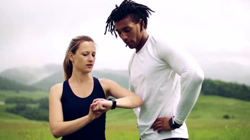 Young Couple Using Smartwatch After Exercise on Meadow Outdoors in Nature