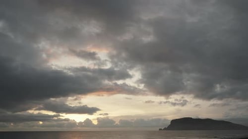 An island in the sea against the backdrop of clouds and the setting sun behind them.