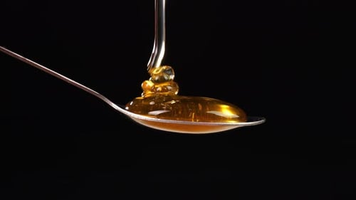 Honey Pouring To Spoon On Black Background. Organic Thick Honey Sweet Dessert
