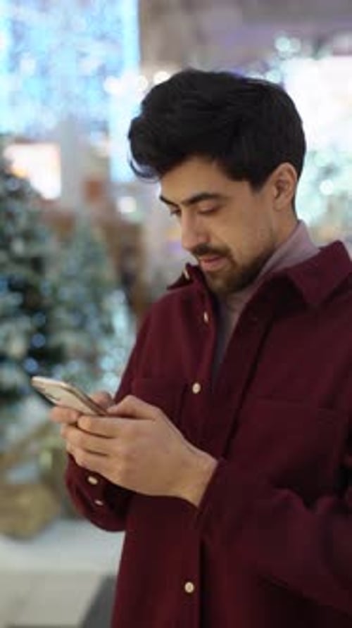 Vertical Portrait of Bearded Young Man Typing Message Using Mobile Phone Looking on Screen Standing