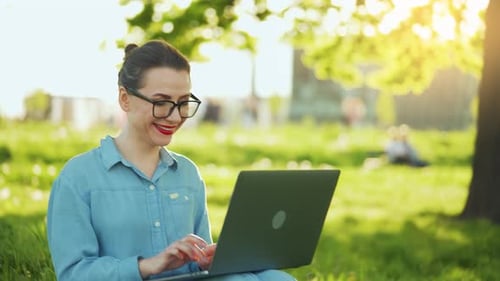 Busy Attractive Woman Working on the Laptop While Sitting on Grass in City Park