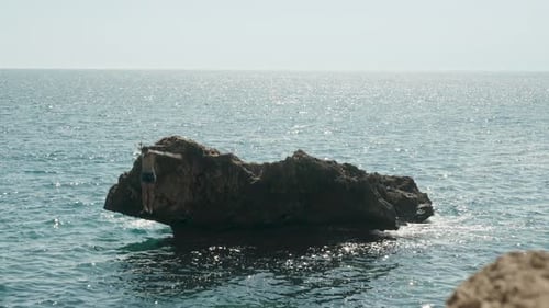 A masked man jumps from a cliff standing in the sea.