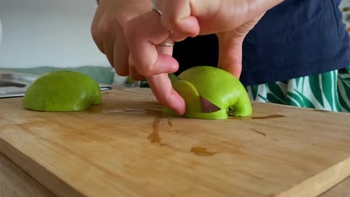 A Woman Demonstrates Her Culinary Skills by Chopping a Fresh Green Apple on a Wooden Cutting Board i