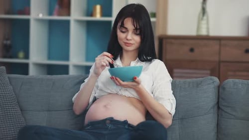 Pregnant Woman Eating Cereal Relaxing on Sofa