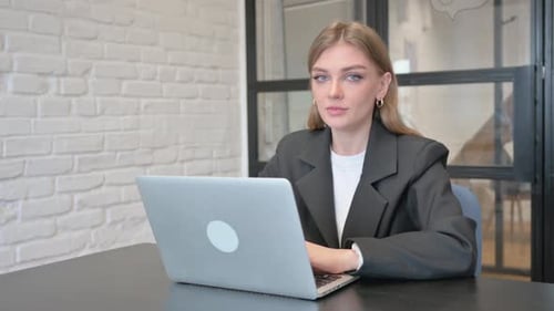 Businesswoman Smiling at Camera while Working on Laptop in Office