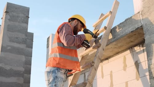 Male construction worker using a drill on a building site with a crane in the background