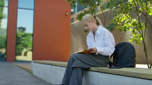Woman Writing in Notebook Outside Modern Urban Building