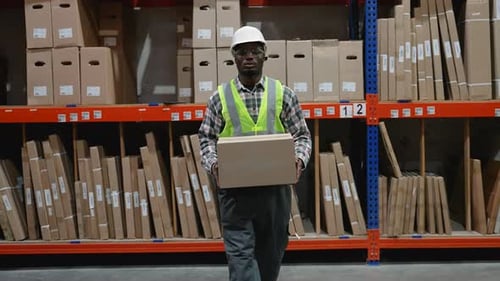 Warehouse Worker Carries Box Toward Camera