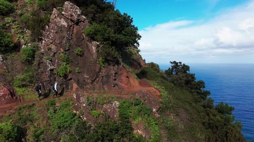 Adventurers Trek Through Narrow Green Cliffside Pathway Overlooking Ocean