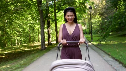 Young Mother Enjoying Walk in Park with Baby Stroller