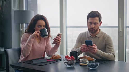Couple Using Phones at Breakfast Table Indoors