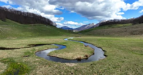 Flug über einen gewundenen Gebirgsbach mit klarem Wasser an einem sonnigen Frühlingstag. Der Bach fließt durch