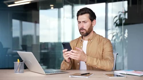 Man looks at phone in office, confused and stressed