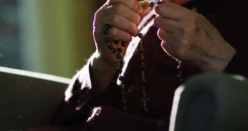 Die Hand einer älteren Frau spricht ein Gebet, indem sie in der Tradition seiner Religion einen Rosenkranz berührt