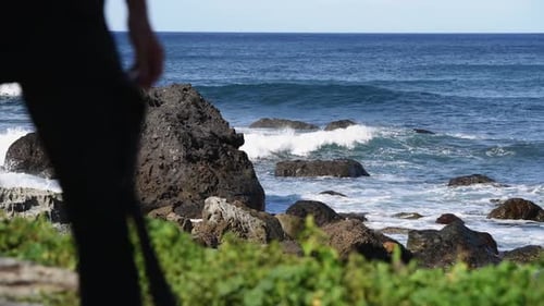 An unrecognizable surfer passes into the ocean water with his board