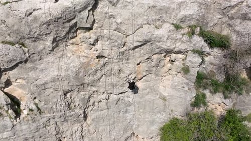 Climber rappelling down cliff with helmet and backpack