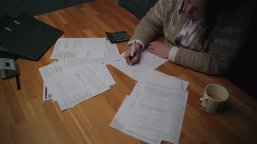 Woman Completes Paperwork at Home on Wooden Table