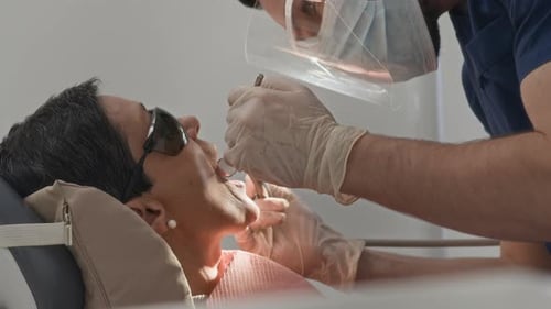 Dentist Examining Patient Teeth with Protective Gear in Modern Clinic