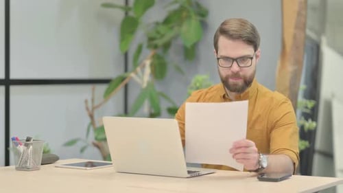 Man Reviews Documents and Works on Laptop