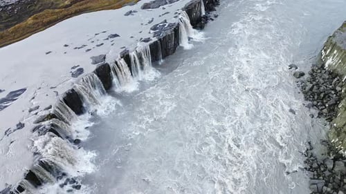 Aerial drone view of Dettifoss waterfall cascading over dark volcanic cliffs. Heavy glacial currents