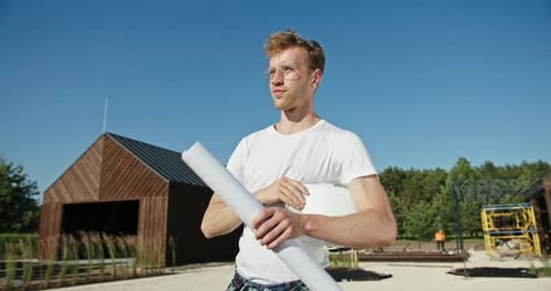 Junger Architekt oder Ingenieur zieht auf einer Baustelle seinen Helm aus, bevor er einen Bauplan ausrollt