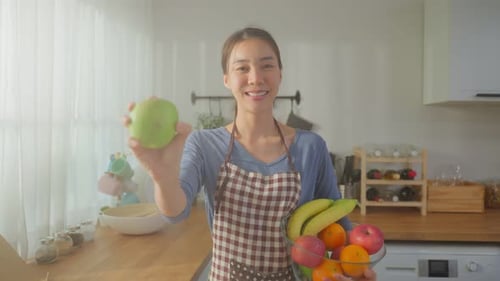 Woman Holds Fruit in Bright Kitchen