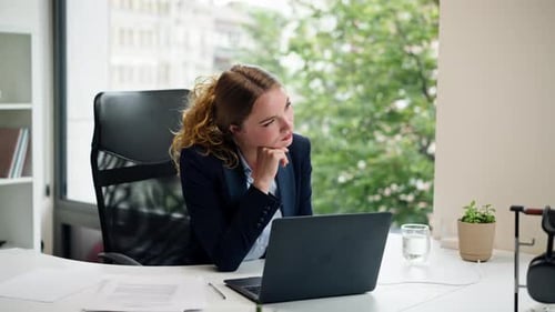 in a Modern Office with a Large Window a Beautiful Worker in a Blue Shirt with a Laptop Looks at the