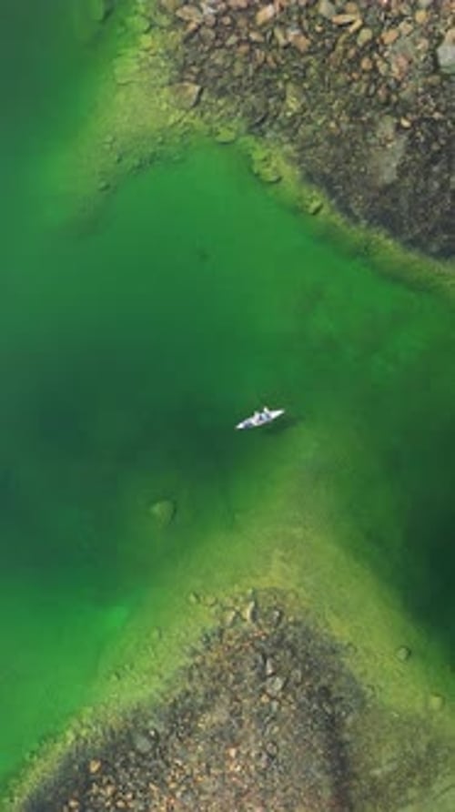 Vertical View Of A Canoe Boat Sailing In Green Lake Lagoon. Aerial Ascending Shot
