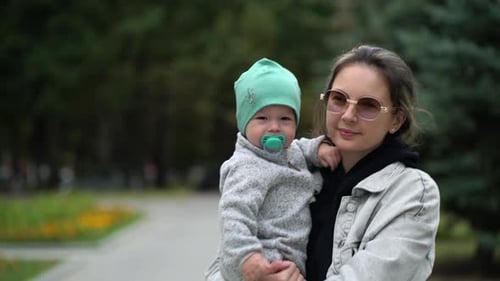Mom Holds Her Little Son in Her Arms During a Family Walk in the Park