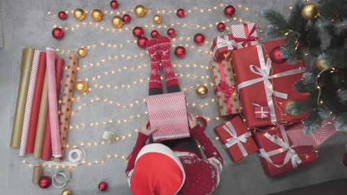 Woman wrapping Christmas present lying on floor overhead