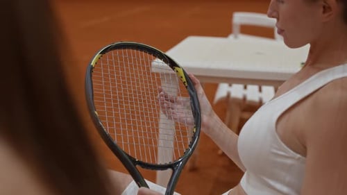 Young Woman Checking Strings of Tennis Racket before Match on Clay Court