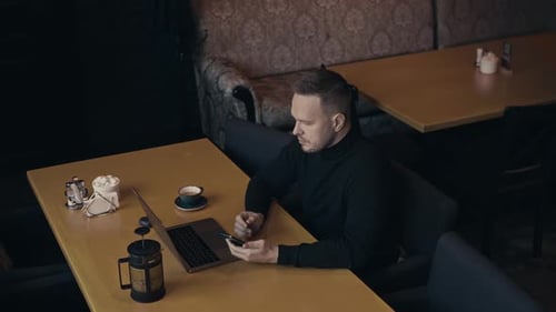 Stylish Male Freelancer Spends Time in a Cafe Drinks a Drink and Works on a Laptop The Workplace Can