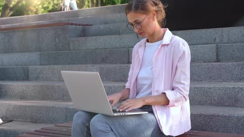 Cheerful Businesswoman Using Laptop Sitting on Steps in Park