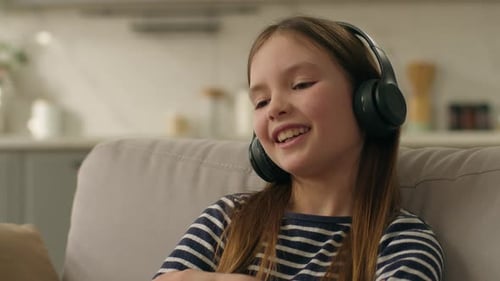 Girl Listens to Music with Headphones on Sofa