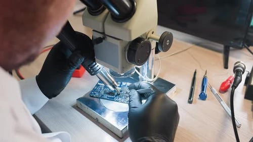 Technicien utilisant un microscope et des outils à souder pour réparer un circuit imprimé