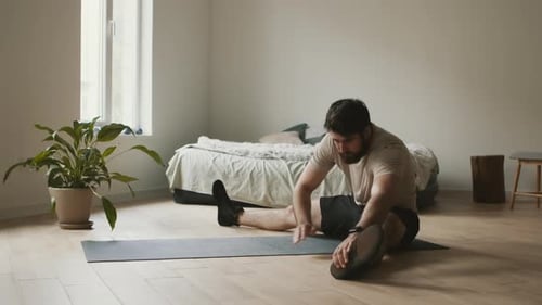 Man Stretching on Yoga Mat in Bedroom