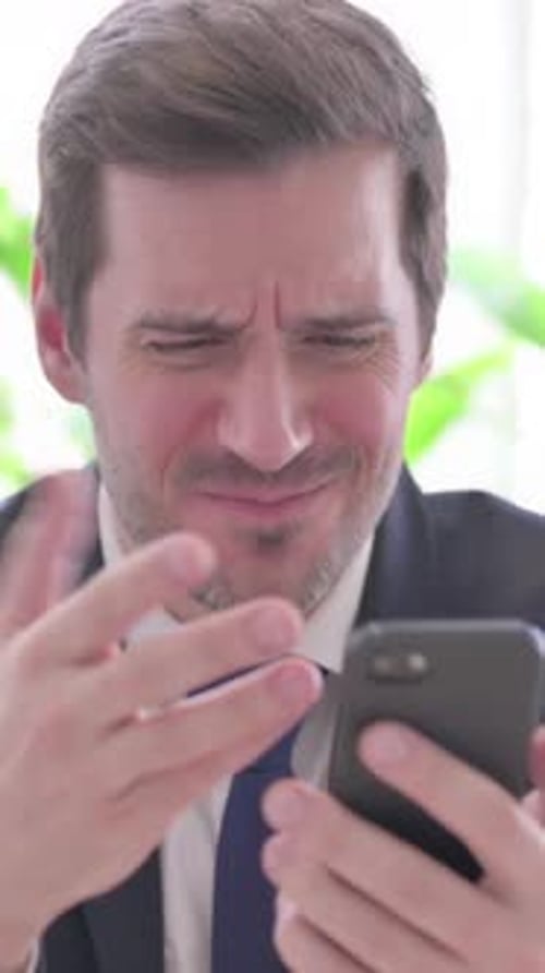Upset Young Businessman Reacting to Loss on Smartphone in Office, vertical video
